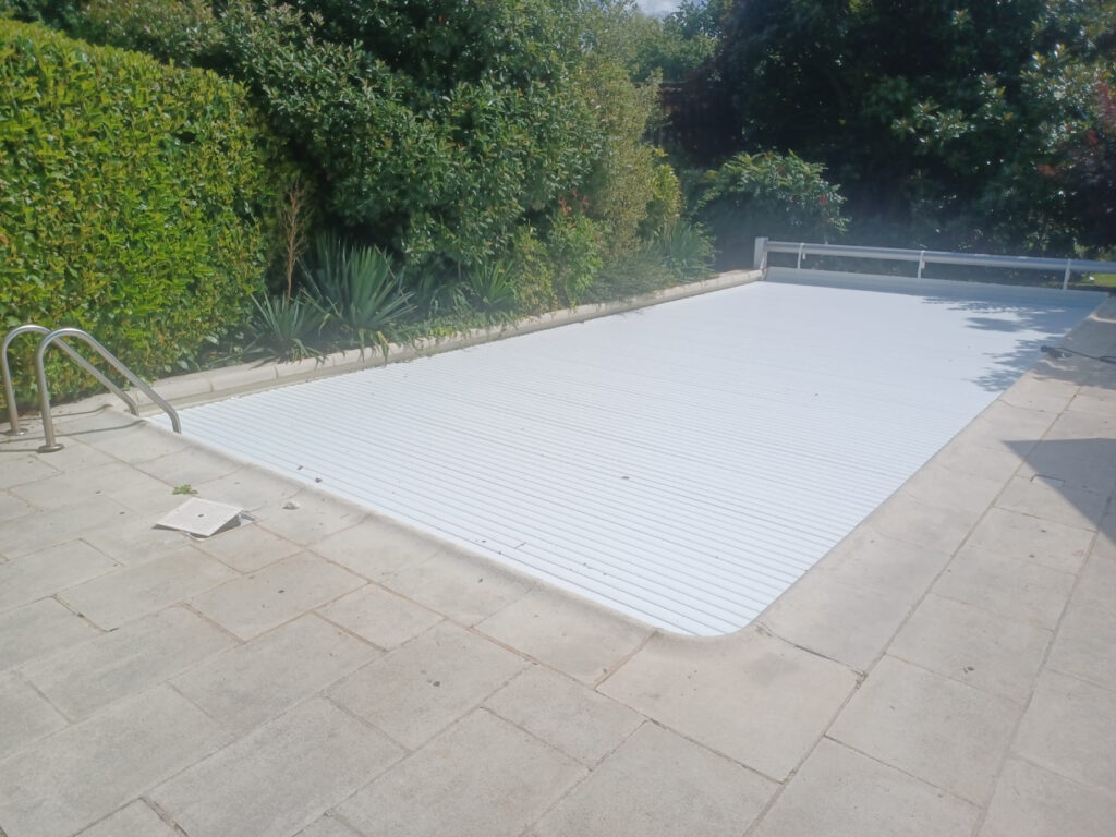 Volet de piscine hors sol à lames blanches déroulé sur un bassin extérieur